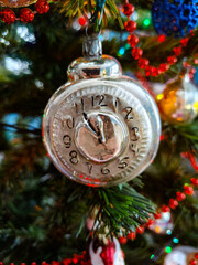 Christmas tree with silver and gold decoration, silver watch, clock, red beads and other decorations in the background. New year