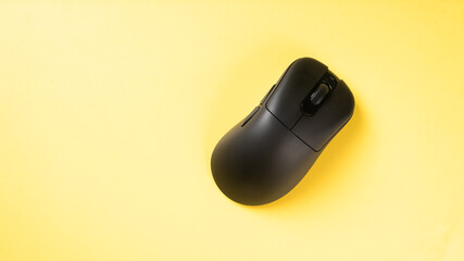A black ergonomic wireless mouse placed on a bright yellow background, showcasing a clean, modern...