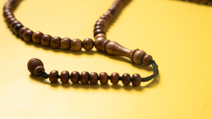 A wooden prayer bead string (tasbih) arranged on a bright yellow background. A spiritual accessory...
