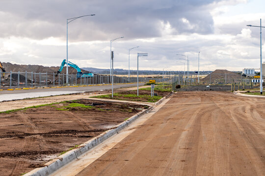 A dusty road and fenced-off construction site in Wyndham Vale, Melbourne, Australia. Residential land development with earthworks, vacant lots, a planned community,and heavy machinery equipment.