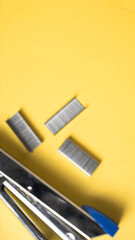 A metal stapler, black-handled scissors, and four staple pieces are arranged on a bright yellow...