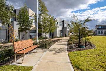 A landscaped footpath in a modern suburban community with newly built townhouses, young trees, and...