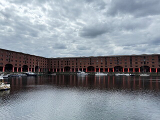 Royal Albert Dock in Liverpool on a cloudy day, with reflections of historic buildings and moored...