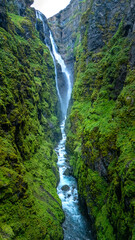 Majestic waterfall cascading through lush green canyon in Icelands breathtaking landscape © Fokke Baarssen