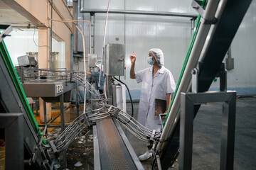 Inspector examines equipment. Manufacturing plant setting. Worker wears hairnet, mask, lab coat. Conveyor systems moving, Clean room environment