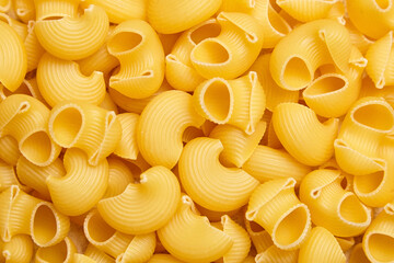 Overhead macro image of dry yellow pipe rigate pasta with ribbed, curved shapes and hollow centers,...