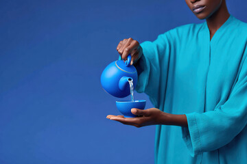 Woman pouring water from blue teapot into blue bowl on blue background