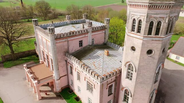 Historic Vecauce Palace with towers and pink facade stands in Latvian landscape