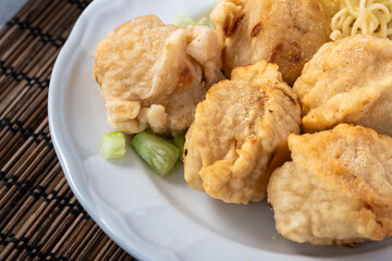 Close-up of crispy Asian pempek adaan served on a white plate with chopped cucumber on the side, placed over a bamboo mat background for an authentic culinary presentation