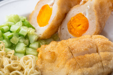 Close-up of Indonesian pempek with salted egg filling, served with diced cucumber and noodles. A savory traditional dish from Palembang, showcasing rich texture and golden crust