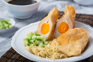 Indonesian pempek kapal selam filled with boiled egg yolk, served with noodles, cucumber, and vinegar sauce. A delicious traditional Palembang dish on a white plate with natural garnish