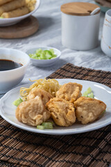 Close-up of traditional Indonesian fried pempek served with yellow noodles, chopped cucumber, and spicy dark vinegar sauce. A savory Palembang street food delicacy