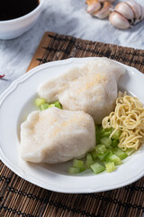 Traditional Indonesian pempek served with diced cucumber, yellow noodles, and spicy vinegar sauce on the side. A savory delicacy made from fish and tapioca