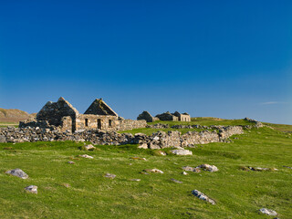 A solitary, abandoned stone cottage stands serenely in the lush green expanse of Collaster, Unst,...