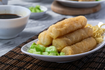 A serving of fried pempek lenjer, traditional Indonesian fishcake, arranged with noodles and diced...
