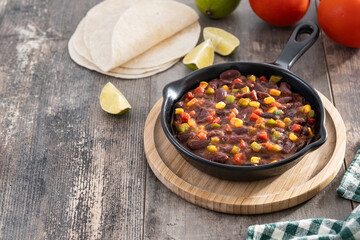 Mexican chilli beans with vegetables in iron pan on wooden table. Copy space