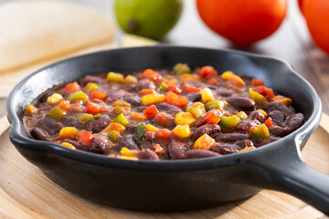 Mexican chilli beans with vegetables in iron pan on wooden table