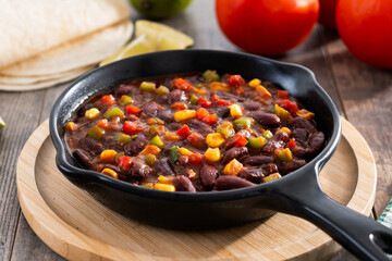 Mexican chilli beans with vegetables in iron pan on wooden table
