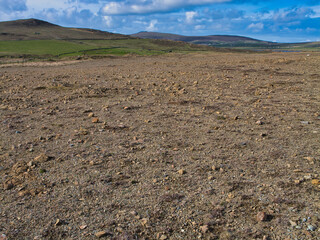 A wide view of the rocky, barren landscape of Keen of Hamar SSSI in Shetland, UK under a bright blue sky.
