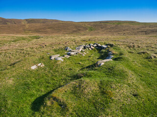 A view of a traditional boat noost at Collaster, Unst, Shetland, set against a vast grassy landscape under a clear blue sky.