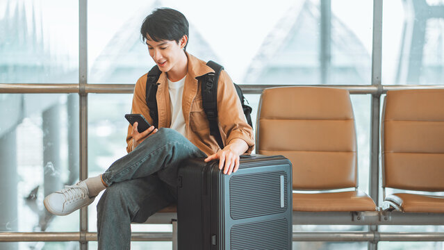 Happy asian tourist man using mobile smartphone with suitcase traveling between waits for flight in Airport Terminal, Browse Internet, flight check in, Tourist journey trip concept, copy space