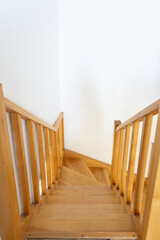 Interior wooden staircase with railing and white walls in residential home.
