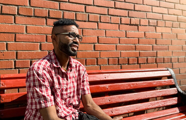 Portrait of a young man of African-American nationality wearing glasses with a beard sitting on a...
