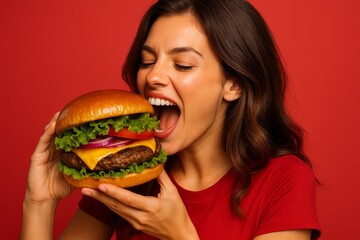 Young woman excited about giant burger savoring anticipation on vibrant red backdrop