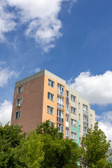 Colorful residential apartment building with multiple windows and textured facade above green trees...