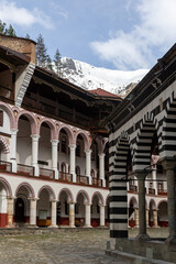 Architectural Detail of Rila Monastery with Snow-Capped Mountains and Striped Archways in Bulgaria