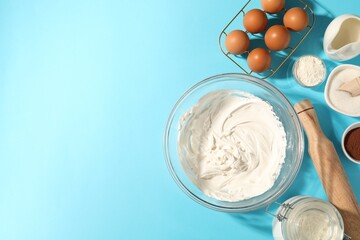 Whipped cream in bowl and other products on light blue table, flat lay. Space for text