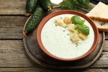 Tasty cucumber soup with croutons, basil, bread and vegetables on wooden table, closeup