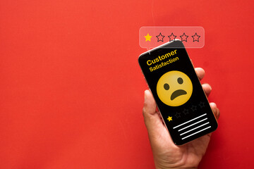 Bad customer review concept. A hand holds a smartphone showing a one-star rating and a sad emoji on...