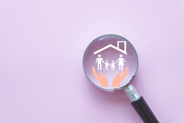 Family life insurance concept. A magnifying glass focuses on an icon of hands protecting a family...