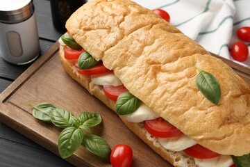 Tasty sandwich with mozzarella cheese, tomatoes and basil on black wooden table, closeup