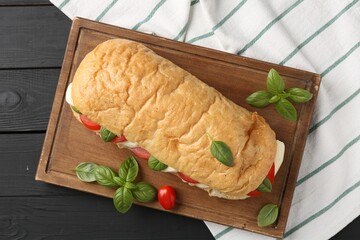 Tasty sandwich with mozzarella cheese, tomatoes and basil on black wooden table, top view