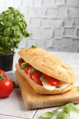 Tasty sandwich with mozzarella cheese, tomatoes and basil on light tiled table against grey...