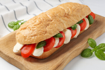 Tasty sandwich with mozzarella cheese, tomatoes and basil on white table, closeup