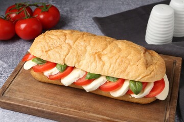 Tasty sandwich with mozzarella cheese, tomatoes and basil on grey textured table, closeup