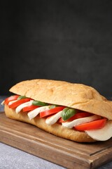 Tasty sandwich with mozzarella cheese, tomatoes and basil on grey textured table against dark...