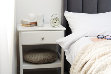 Bedside table with alarm clock and decor near bed indoors