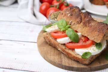 Tasty sandwich with mozzarella cheese, tomatoes and basil on white wooden table, closeup. Space for text