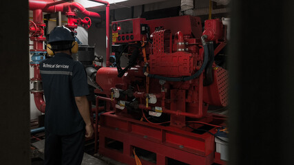 A technician inspects a red fire pump in a confined, dark space.
