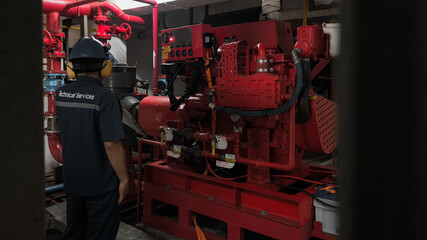 A technician inspects a red fire pump engine in a confined space.