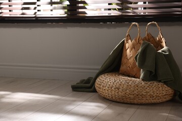 Wicker pouf and basket with plaid at home. Space for text