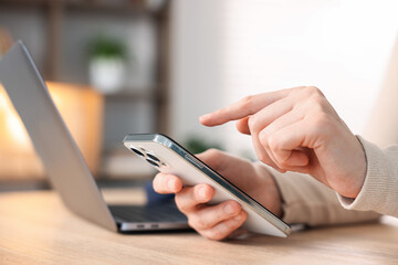 Woman using modern smartphone at wooden table indoors, closeup