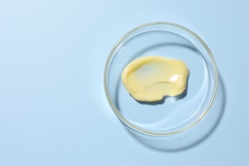 Cosmetic product in Petri dish on light blue background, top view. Space for text