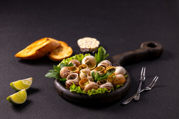 Cooked snails with garlic butter and herbs served on wooden board