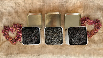 View from above of square metal jars filled with organic loose leaf tea, arranged on a burlap...