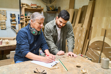 Experienced craftsman instructing young apprentice in woodworking shop